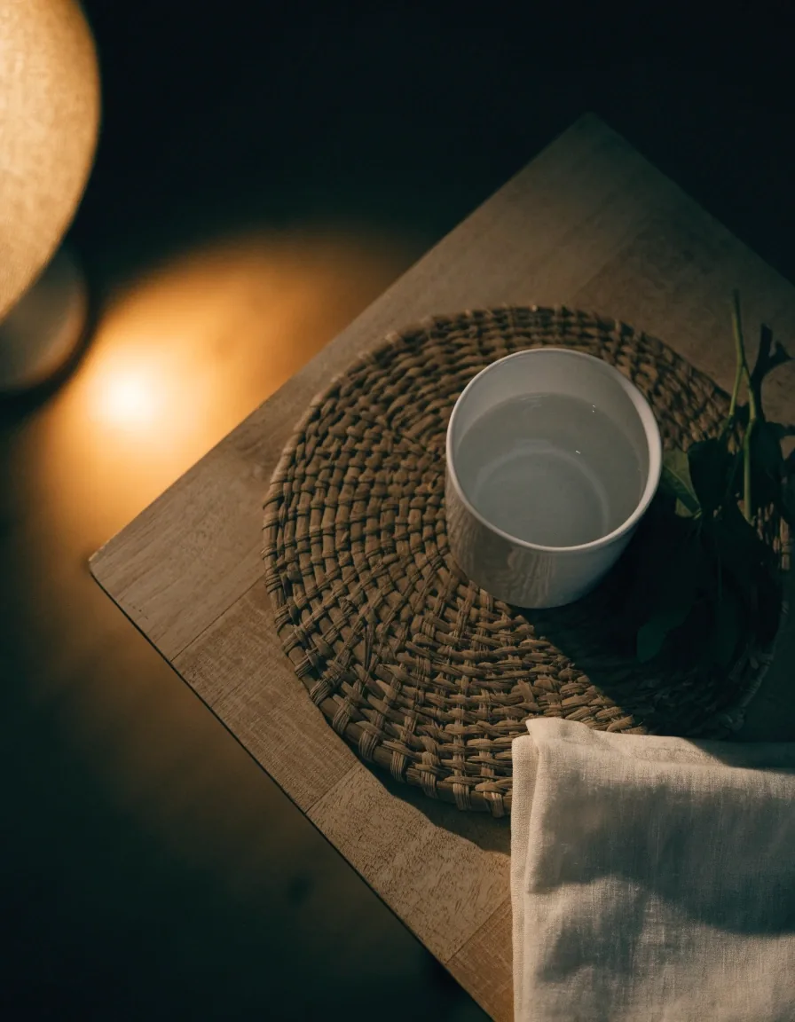 An overhead view of a consult table with a notebook, cup and sprig of greens under a warm lamp